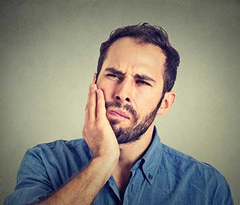 unhappy troubled handsome bearded man touching his cheek he has toothache isolated on gray background