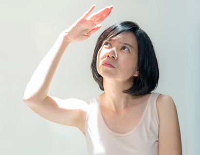 Girl with short black hair covering face by hand from bright sun light