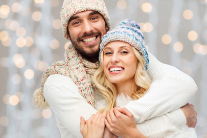 Happy couple in winter clothes hugging over lights