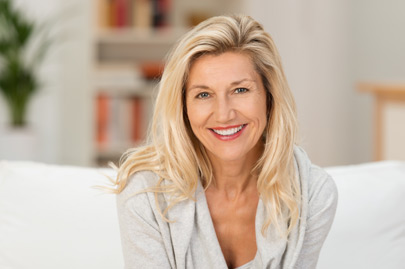 Lovely middle-aged blond woman with a beaming smile sitting on a sofa at home looking at the camera