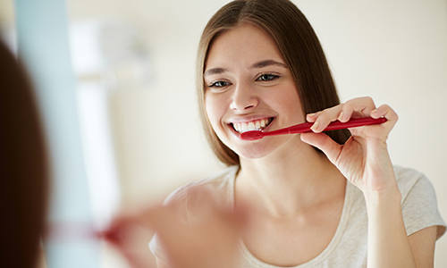Yooung woman brushing her teeth at mirror
