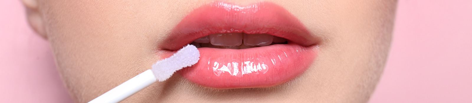 Beautiful young woman applying gloss on her perfect lips